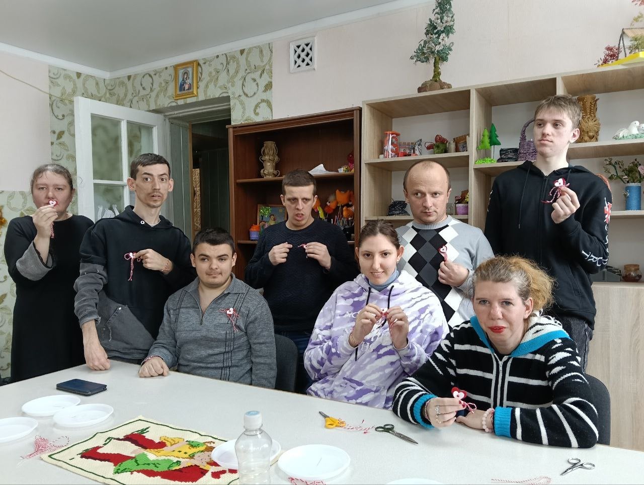 Участники показывают небольшие красно-белые поделки у стола в мастерской